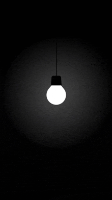 a white light bulb hanging from a ceiling in the dark .