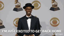 a man in a suit and bow tie stands in front of a wall of grammy awards with the caption i 'm just excited