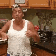 a woman in a white tank top is standing in a kitchen with a butterfly on the wall behind her .