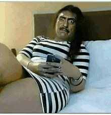 a woman in a striped dress is sitting on a bed holding a cell phone