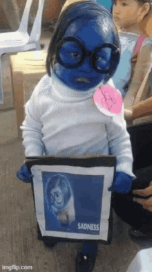 a child dressed in a sadness costume is holding a piece of paper