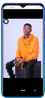 a phone screen shows a pixelated image of a man wearing an orange hoodie that says mystic