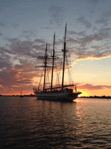 a large sailboat is in the water at sunset with the sun setting behind it