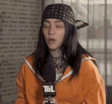 billie eilish is wearing a bandana and holding a microphone while talking into it .