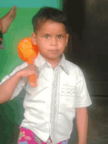 a little boy in a white shirt holds an orange toy