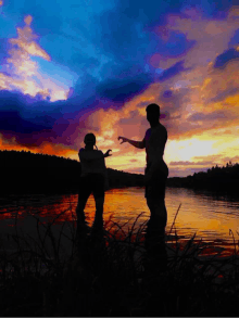 a couple standing in the water at sunset making a heart shape with their hands