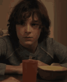 a young boy sitting at a table with a bowl of cereal and a red cup