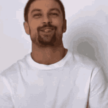 a man with a beard wearing a white t-shirt is smiling with his eyes closed