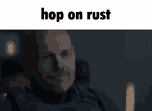 a man with a beard is sitting in a dark room with the words `` hop on rust '' written above him .