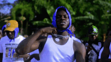 a man wearing a white tank top with a blue bandana around his head stands in front of a crowd