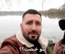 a man with a beard is standing in front of a body of water with a caption in a foreign language