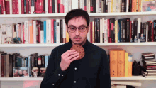 a man is eating a cookie in front of a bookshelf that has a book titled ' a brief history of time '