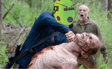 a man wearing a green mask is holding a dead zombie