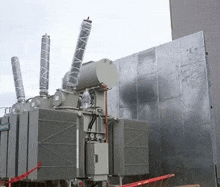 a large transformer is sitting in front of a building with a metal wall behind it .