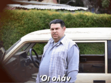 a man in a plaid shirt stands in front of a car with the word " oioaay " on the bottom