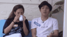 a woman drinking from a cup next to a man wearing a ralph lauren shirt