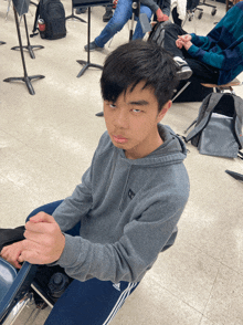 a young man wearing a grey adidas hoodie sits on the floor