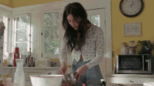 a woman is mixing something in a bowl in a kitchen with a clock on the wall that shows the time as 10:10