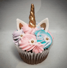 a unicorn cupcake with pink and blue frosting and a gold horn