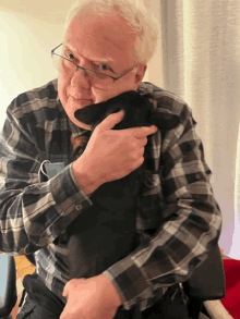 a man wearing glasses is holding a black dog