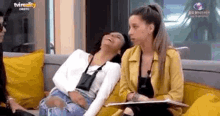 two women are sitting next to each other on a couch laughing .