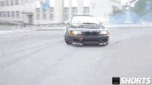 a black bmw m3 is drifting down a street in front of a building .