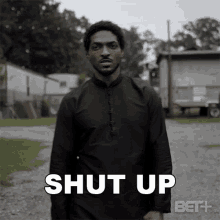 a man in a black shirt is standing in a gravel driveway with the words shut up written on his chest