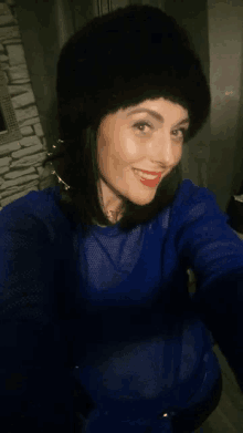 a woman wearing a blue shirt and a black hat is taking a selfie