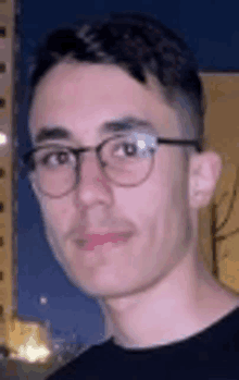 a young man wearing glasses is standing in front of a building at night .