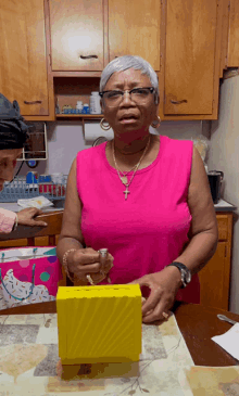 a woman in a pink tank top with a cross necklace is holding a yellow box