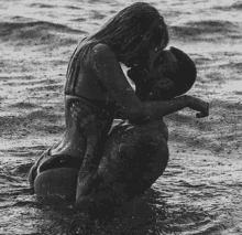 a black and white photo of a man and a woman kissing in the ocean .