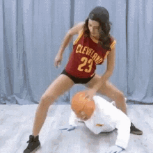 a woman in a cleveland jersey is kneeling on a man in a white shirt while holding a basketball .