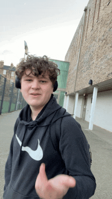 a young man wearing headphones and a nike sweatshirt stands in front of a brick building