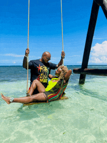 a man and a woman are swinging in the water and the man is wearing a shirt that says one love hai