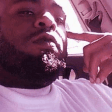 a man with a beard is taking a selfie in a car with his hand on his face .