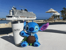 a stitch stuffed animal sits next to a msc cruise cup