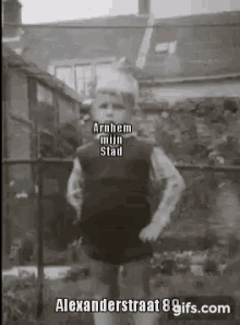 a black and white photo of a young boy standing in front of a fence with the caption arnhem mijn stad .