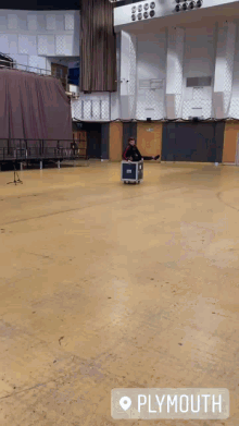 a man is pushing a box on a cart in an empty auditorium with plymouth written on the bottom right