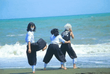 three people are standing on a beach with one wearing a black shirt with chinese writing on the back