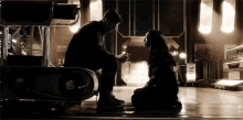 a man is kneeling down next to a woman in a dark room holding a ring .