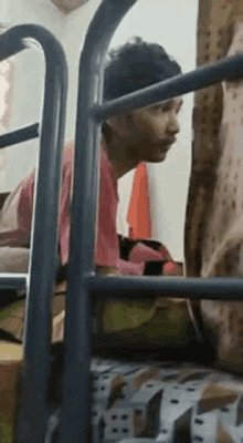 a man in a pink shirt is sitting on a bed in a dorm room .