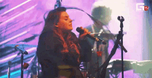 a woman is singing into a microphone on stage in front of a purple background .