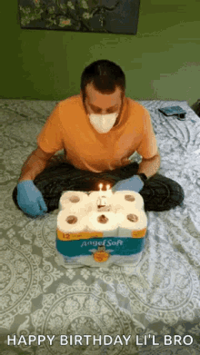 a man wearing a mask and gloves is sitting on a bed with a birthday cake made out of toilet paper