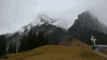 a windmill sits on a grassy hillside in front of a mountain