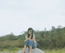 a woman is sitting on a rock in a field