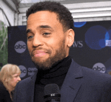 a man in a suit and black turtleneck is talking into a microphone in front of an abc sign