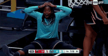 a basketball player is sitting on the floor with his hands on his head in front of a scoreboard that says the app