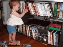 a little girl is standing in front of a shelf full of dvds including one that has the number 3 on it