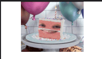 a slice of cake with a face on it and balloons in the background