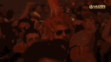 a man wearing sunglasses and a red mohawk is dancing in a crowd of people at a music festival .